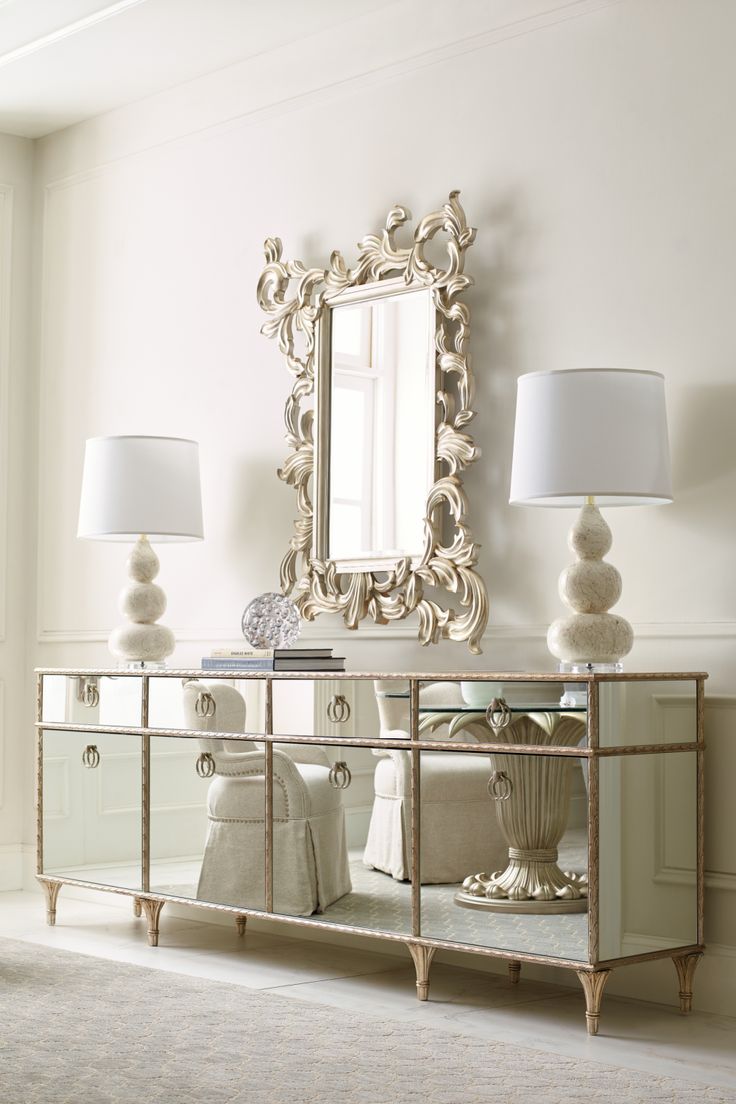 a white room with a mirror and two lamps on the sideboard in front of it