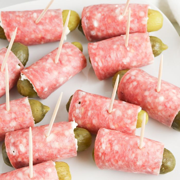 several pickles wrapped in ham and cheese on a white plate with toothpicks