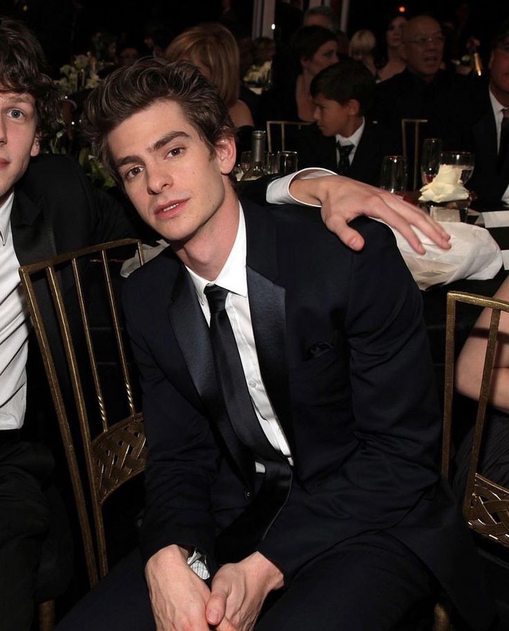 two young men sitting next to each other in front of a table full of people