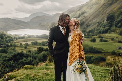 a bride and groom kissing on the side of a lush green hillside with mountains in the background