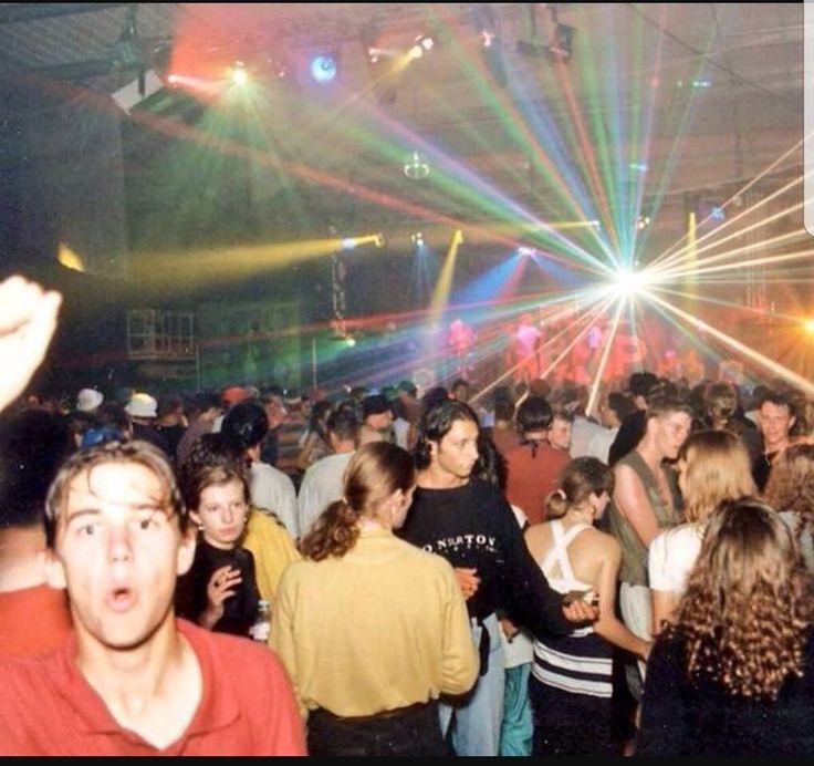 a large group of people standing around in a room with bright lights on the ceiling