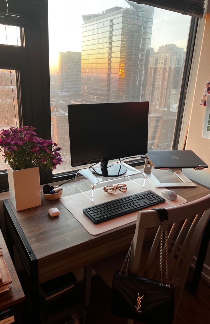 a desk with a computer on it in front of a large window overlooking the city