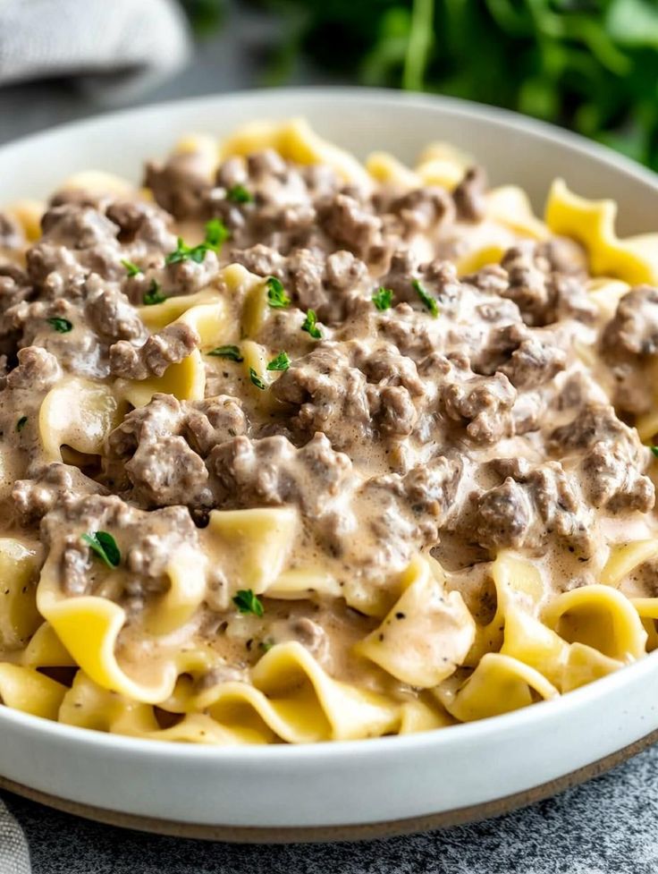 a white bowl filled with pasta covered in ground beef and gravy on top