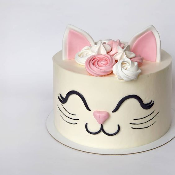 a white cake with pink and white flowers on top, decorated with a cat's face