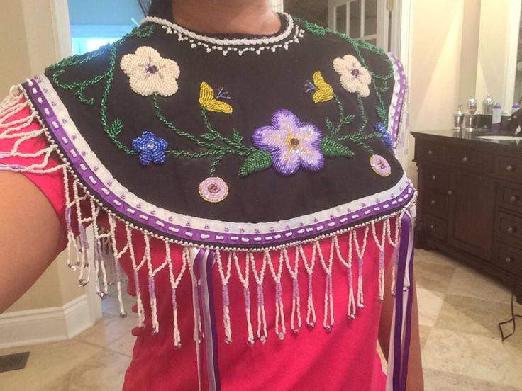 a woman wearing a black and pink dress with flowers on it's chest, standing in front of a mirror