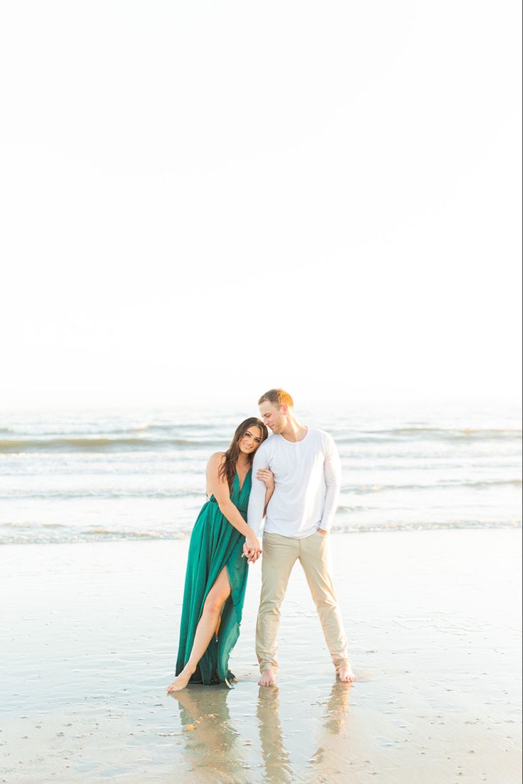 an engaged couple standing on the beach with their arms around each other