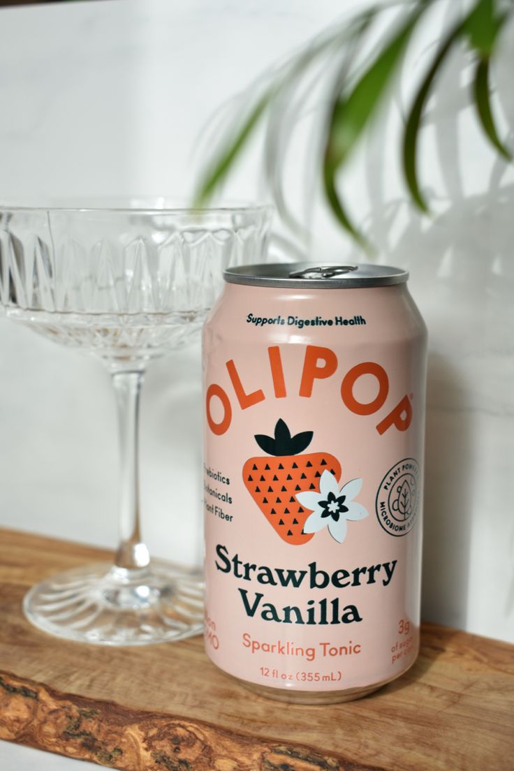 a can of strawberry vanilla sitting next to a martini glass on a wooden counter top