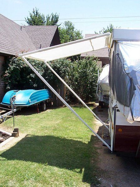 a boat that is sitting in the grass next to a house with a tarp over it