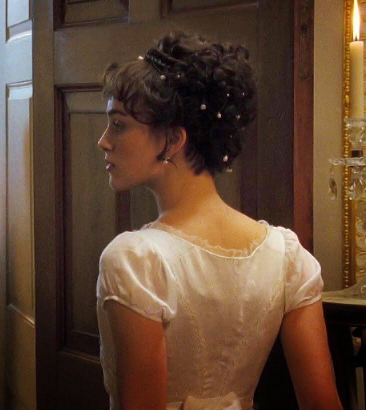 a woman standing in front of a mirror wearing a white dress with pearls on it