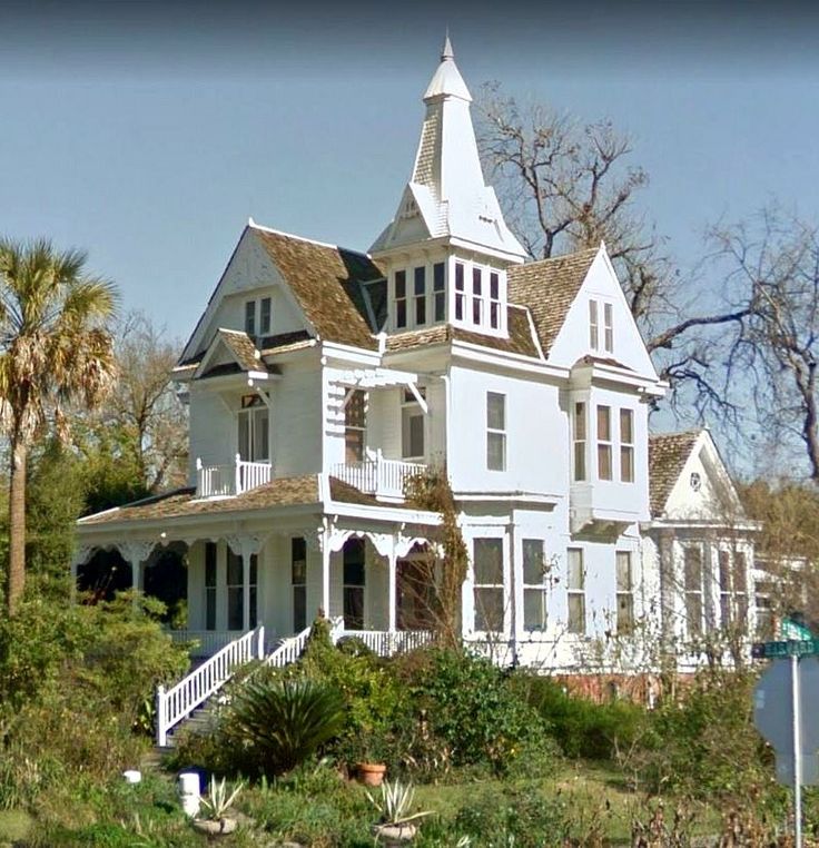 a large white house sitting on top of a lush green hillside next to trees and bushes