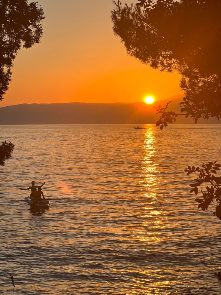 two people on a boat in the water at sunset