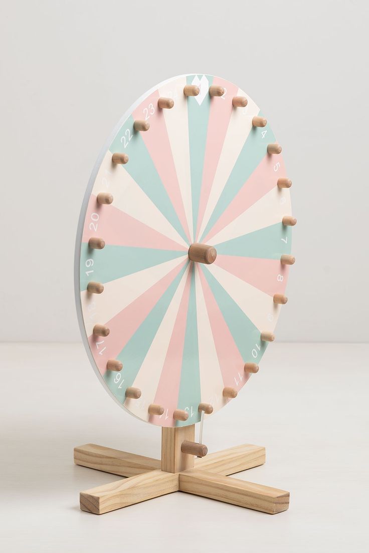 a pink and blue spinning wheel sitting on top of a wooden stand in front of a white wall