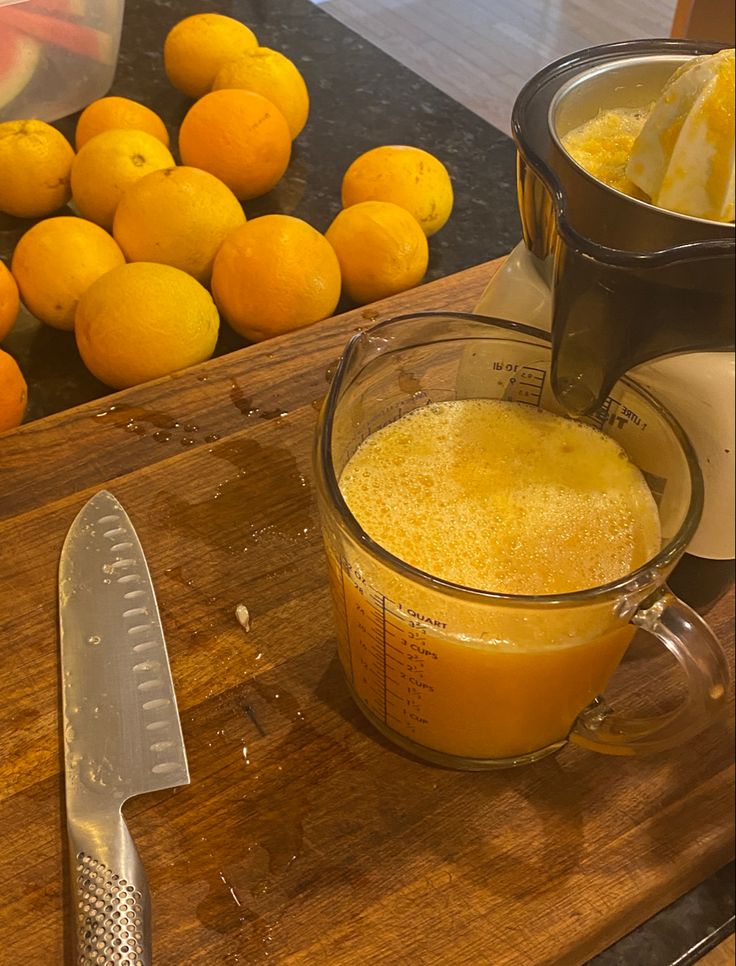 orange juice being poured into a measuring cup on a wooden cutting board next to fruit