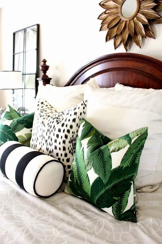 a bed topped with lots of pillows on top of it's headboard next to a mirror