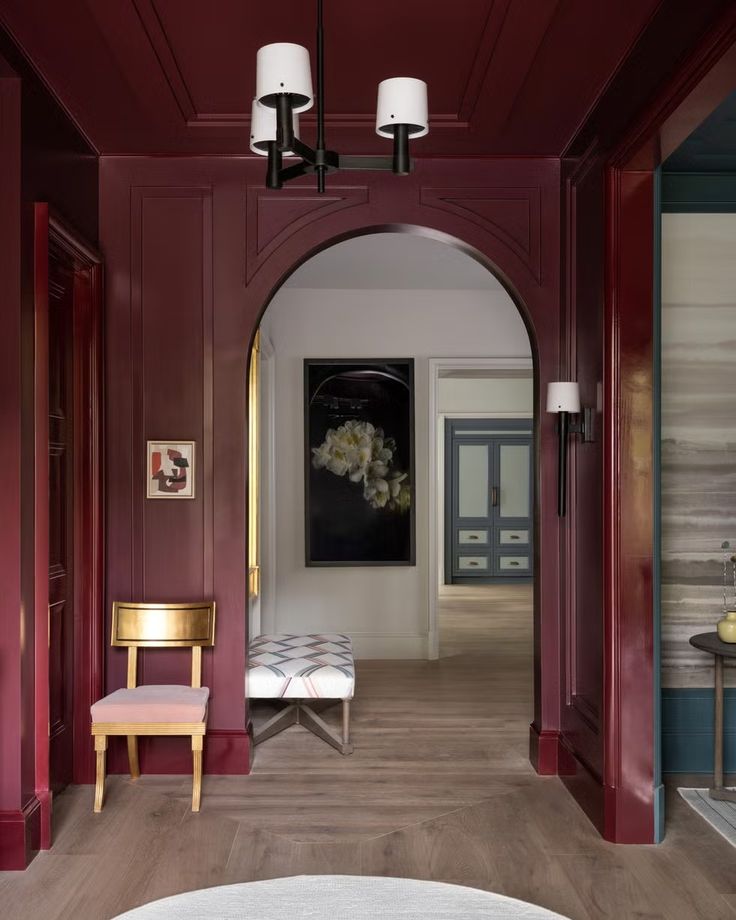 a hallway with red walls and wooden flooring has a bench in the center, along with two lamps on either side