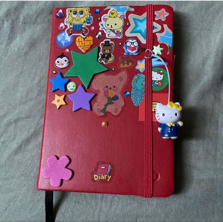 a red notebook covered in lots of stickers and magnets on top of a bed