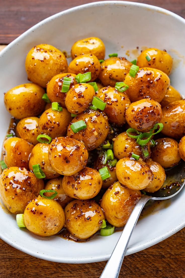 a white bowl filled with cooked potatoes and garnished with scallions on a wooden table