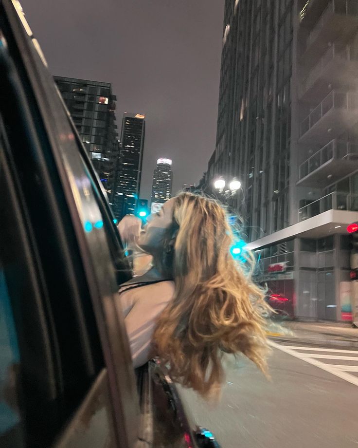 a woman is riding in the back of a car with her head out the window