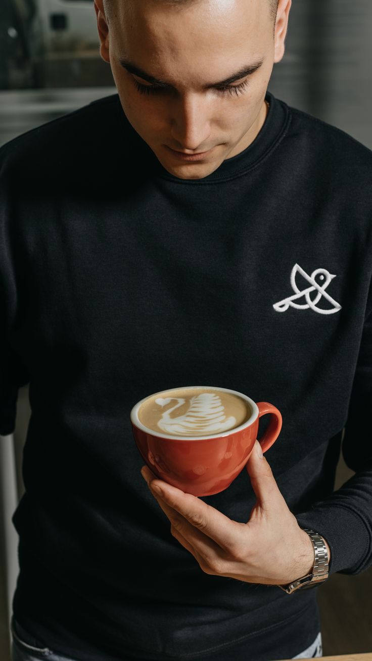 a man holding a cup of coffee in his right hand and looking down at it