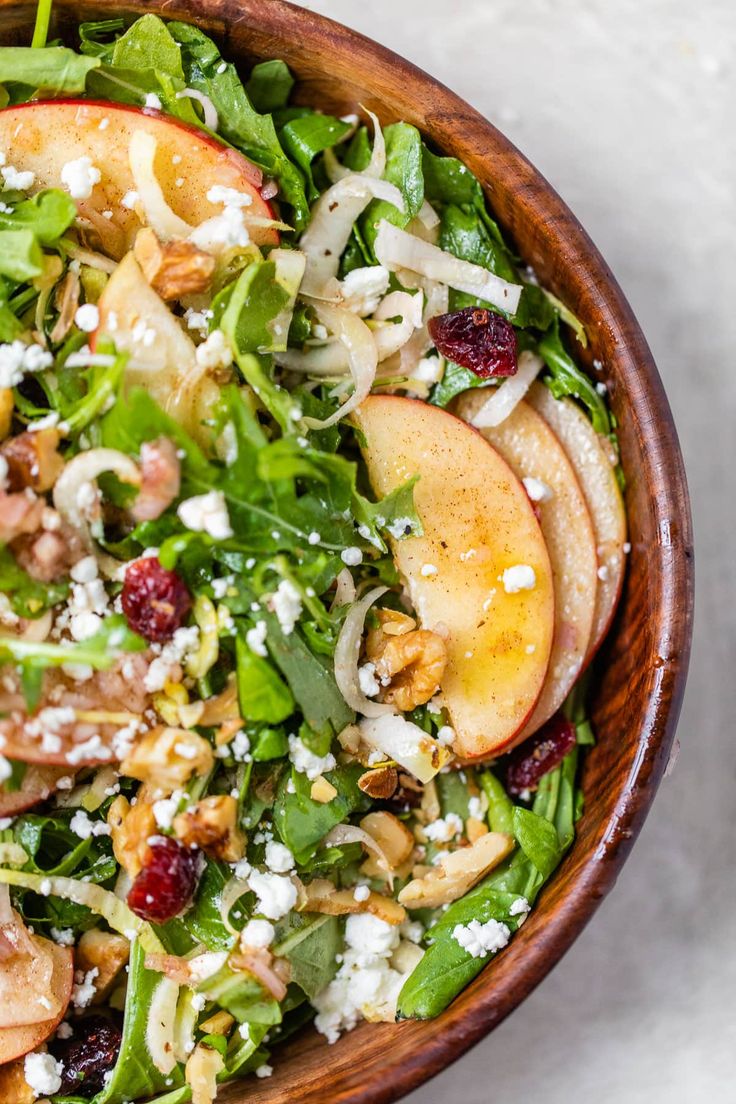 a salad with apples, spinach and feta cheese in a wooden bowl on a white surface