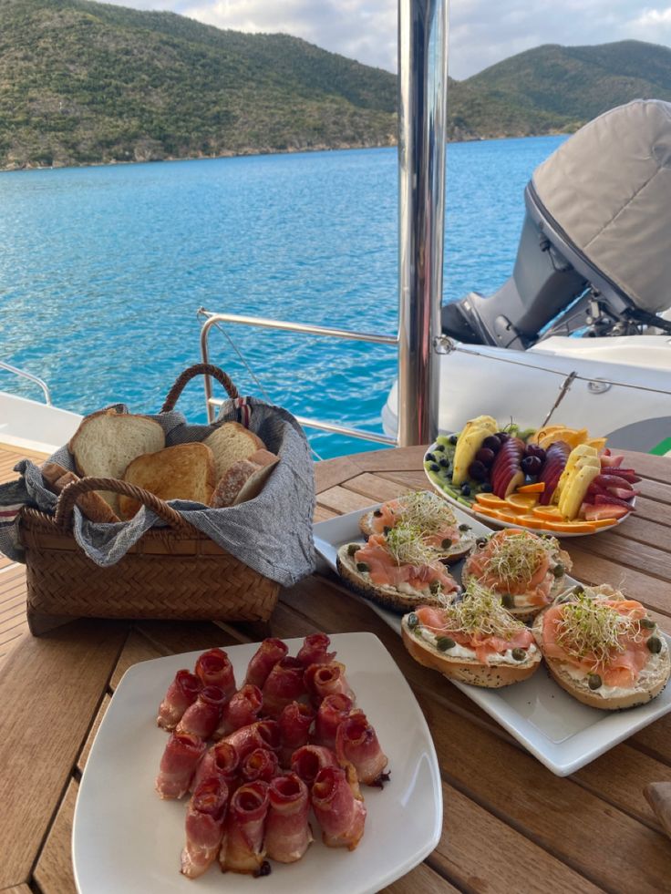 some food is sitting on a table near the water and in front of a boat