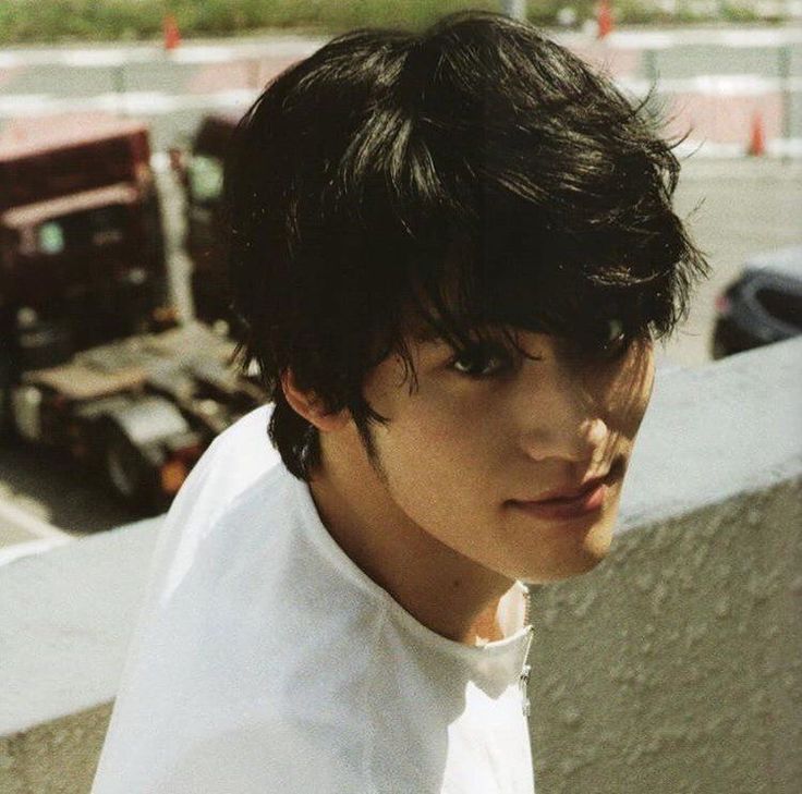 a young man standing next to a truck on the side of a road and looking at the camera