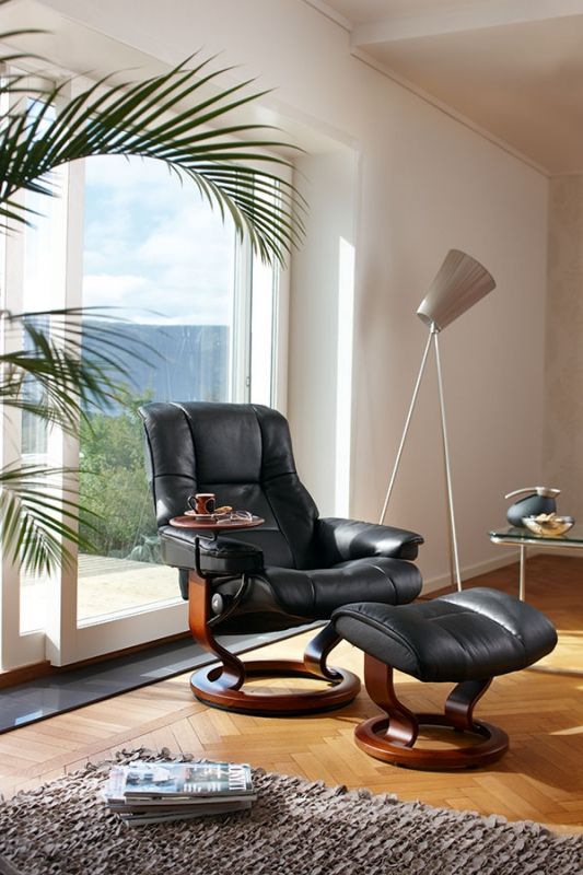 a living room with a chair and ottoman next to a large window overlooking the ocean