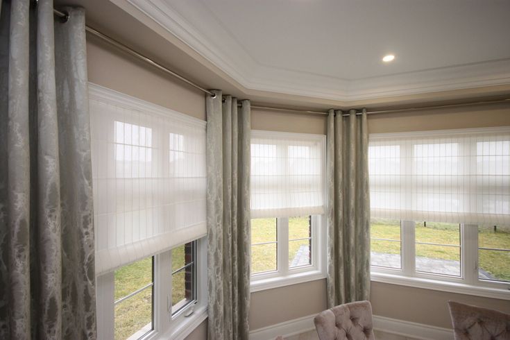 a chair sitting in front of two windows with drapes on the top of them