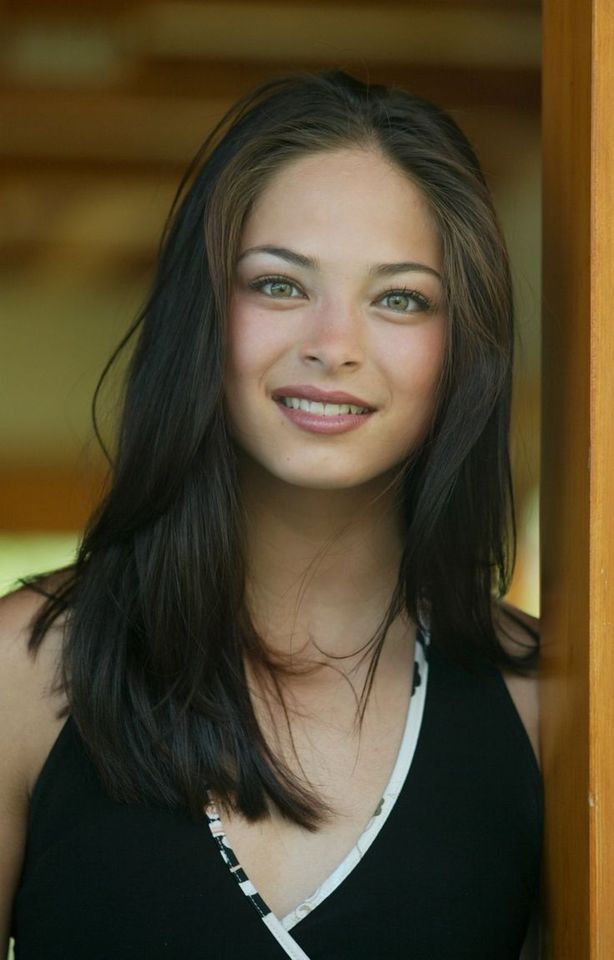 a beautiful young woman standing next to a wooden wall with her eyes closed and looking at the camera