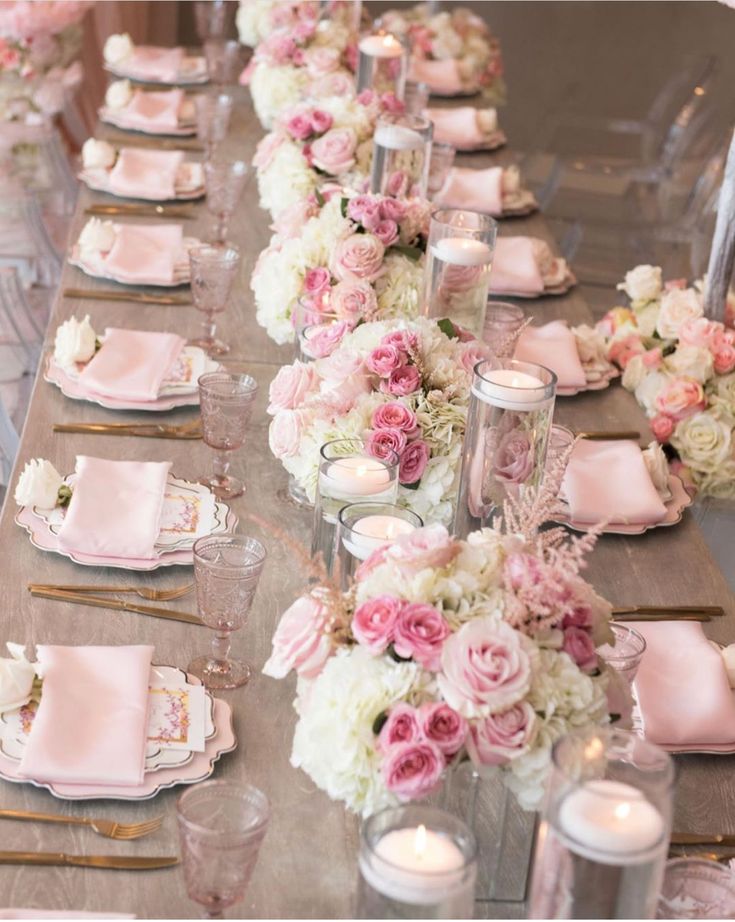 a long table is set with pink and white flowers, candles and napkins on it