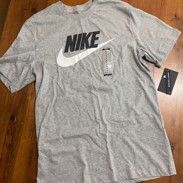 Grey Nike Logo Tshirt Casual Cotton T-shirt In Athletic Heather, Nike Athletic Heather Crew Neck T-shirt, Nike Cotton T-shirt In Athletic Heather, Nike Short Sleeve Pre-shrunk Tops, Nike Cotton Tops For Spring, Tan Graphic Tee With Crew Neck, Gray Crew Neck Top With Logo Print, Tan Graphic Tee Shirt With Crew Neck, Nike Gray Tops With Letter Print