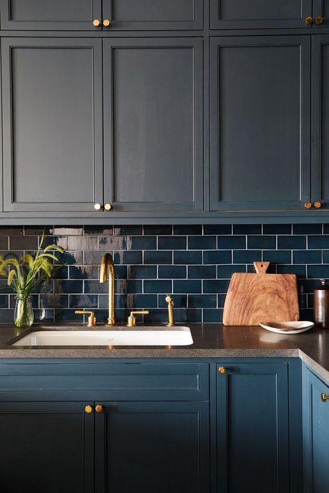 a kitchen with dark blue cabinets and gold pulls on the faucet, white sink and wooden cutting board