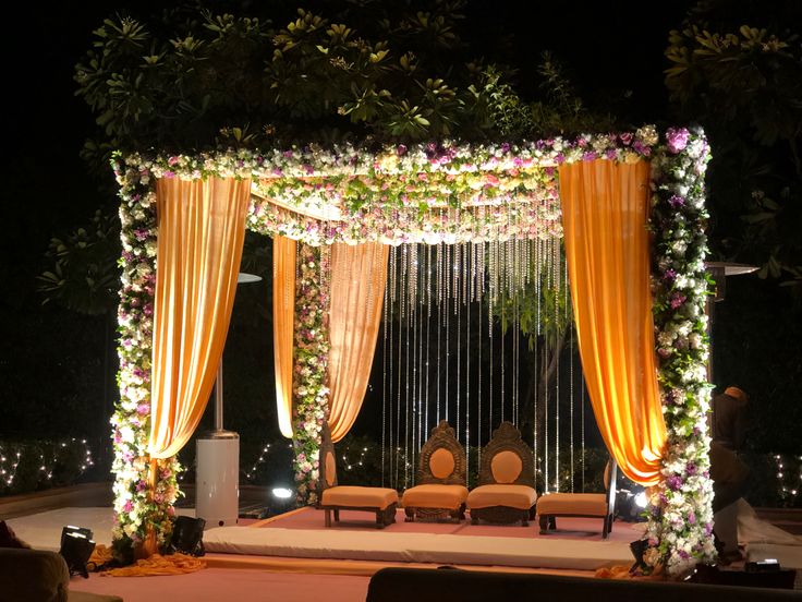 an outdoor wedding setup with orange drapes and white flowers on the stage at night