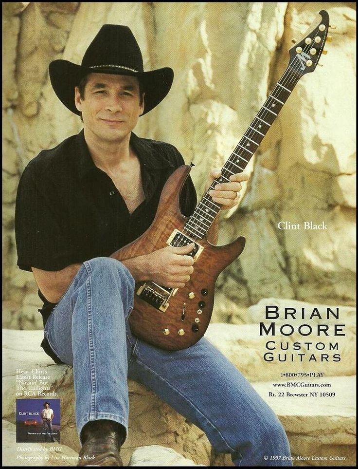 a man sitting on top of a rock with a guitar in his hand and wearing a cowboy hat