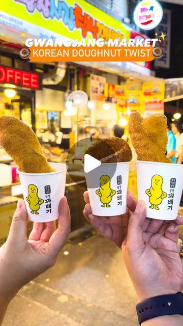 two people holding up cups with fried food in front of a storefront and the words korean doughnut twist written on them