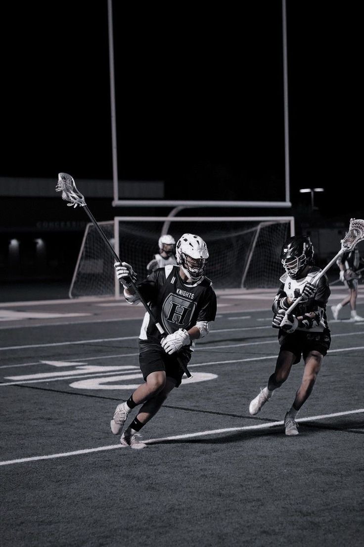 the lacrosse team is playing on an outdoor field at night, with one player in black and white