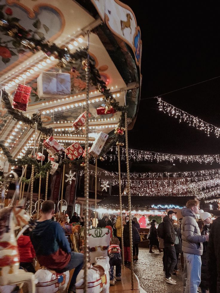 people are walking around an amusement park with lights and decorations on the merry go round