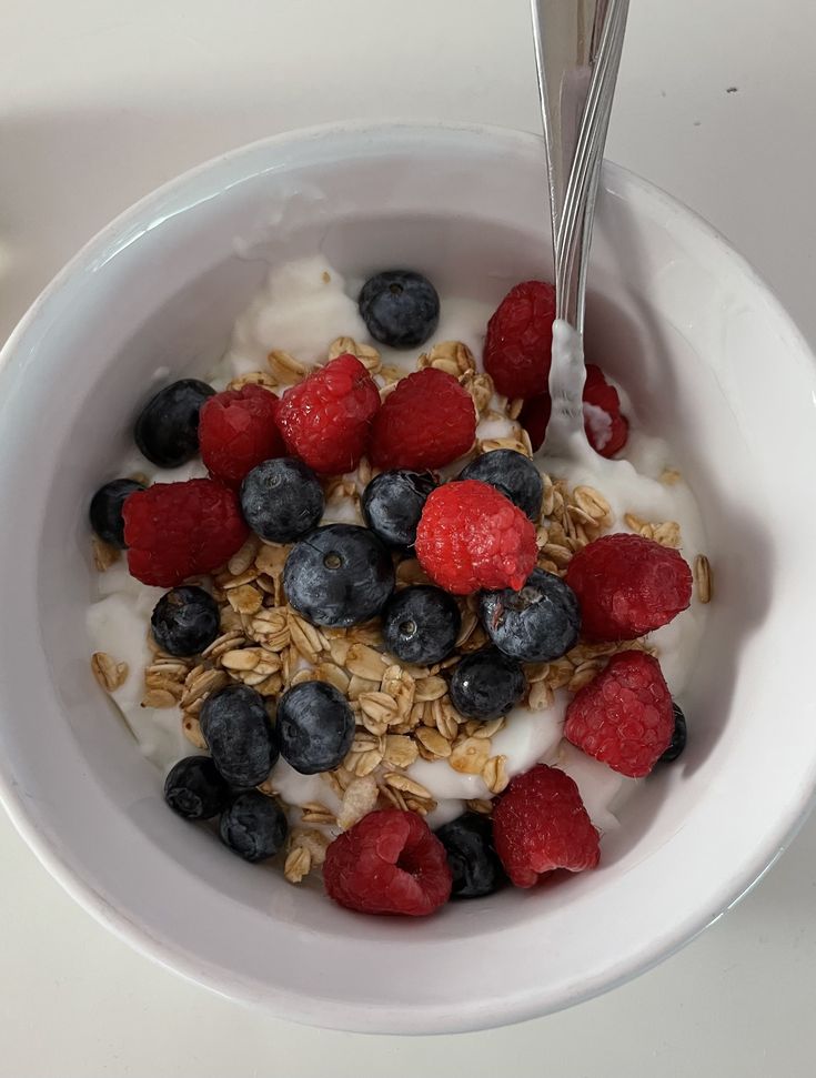 a bowl filled with yogurt, berries and granola on top of a table