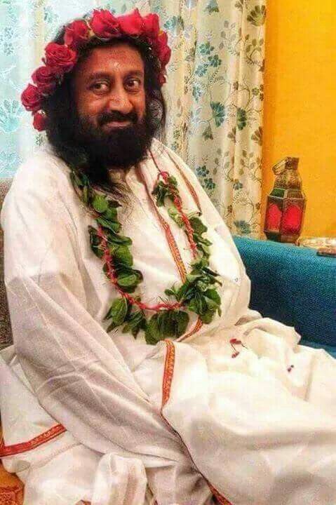 a man with a beard sitting on a couch wearing a flower crown and leis