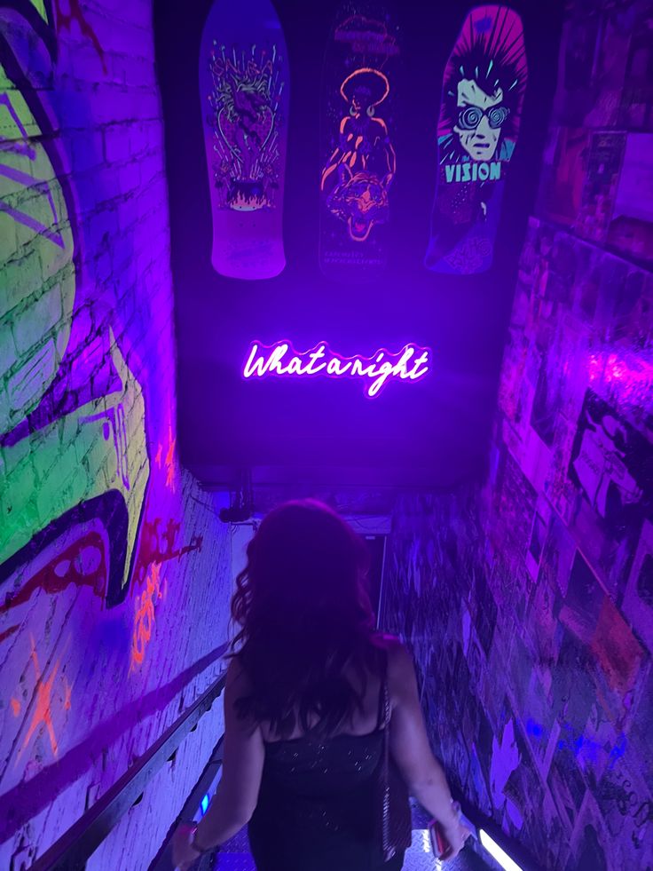 a woman is walking down an escalator in a dark room with neon lights