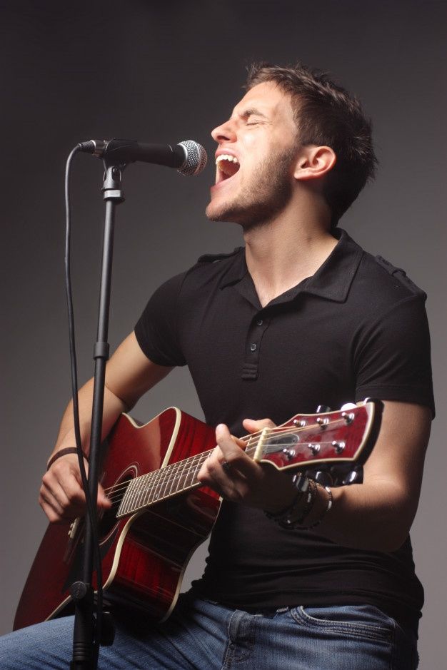 a man singing into a microphone while holding an acoustic guitar in front of his face