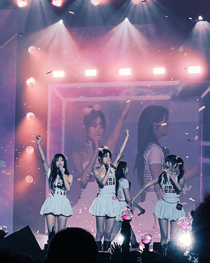 the girls are performing on stage with their arms in the air