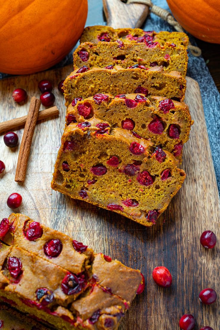 sliced loaf of pumpkin bread with cranberries and cinnamon on cutting board next to pumpkins