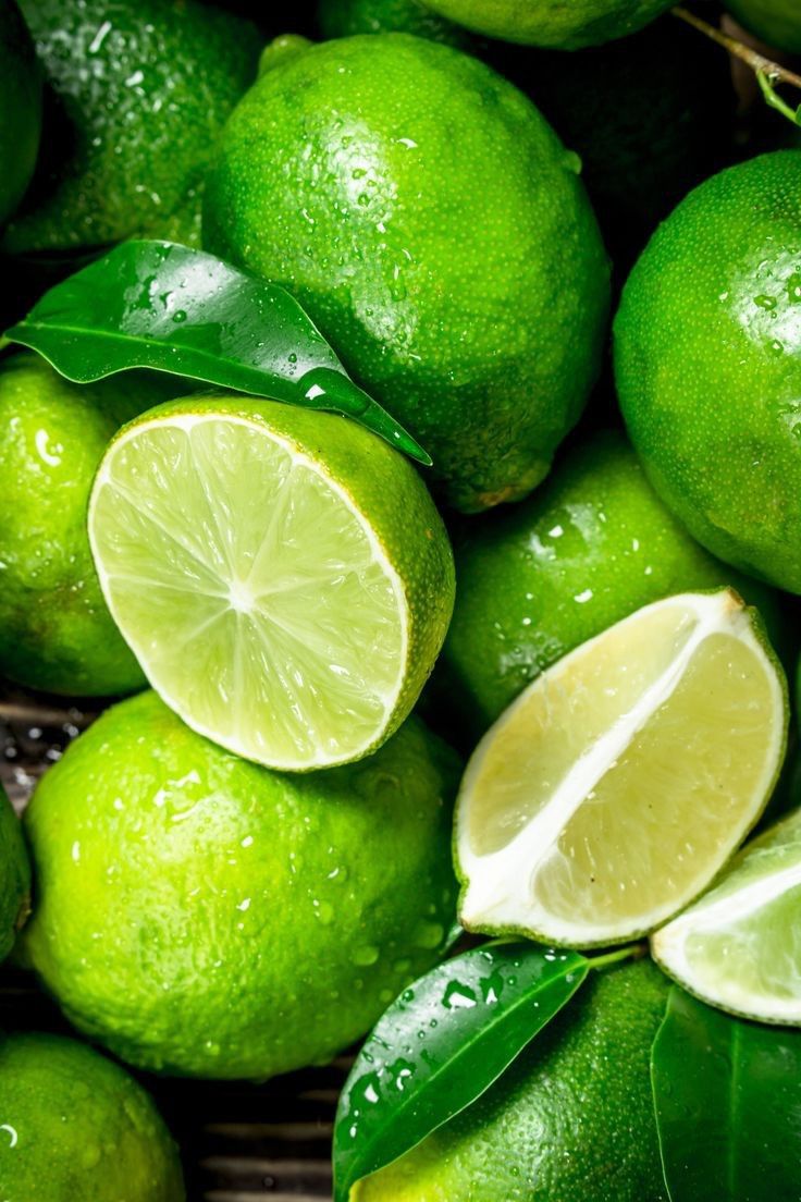 limes with green leaves and water droplets on them are piled up in a pile