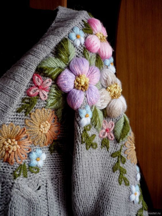 a knitted blanket with flowers and leaves on the edge is sitting on a chair