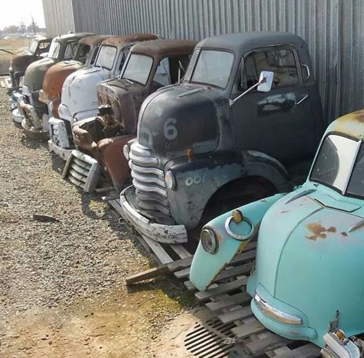 old cars are lined up in a row next to a metal building with a rusted out door