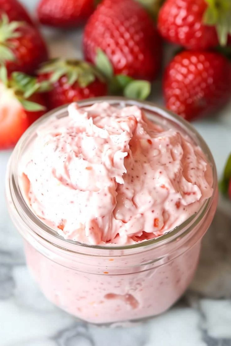 a jar filled with whipped cream next to strawberries on a marble counter top,