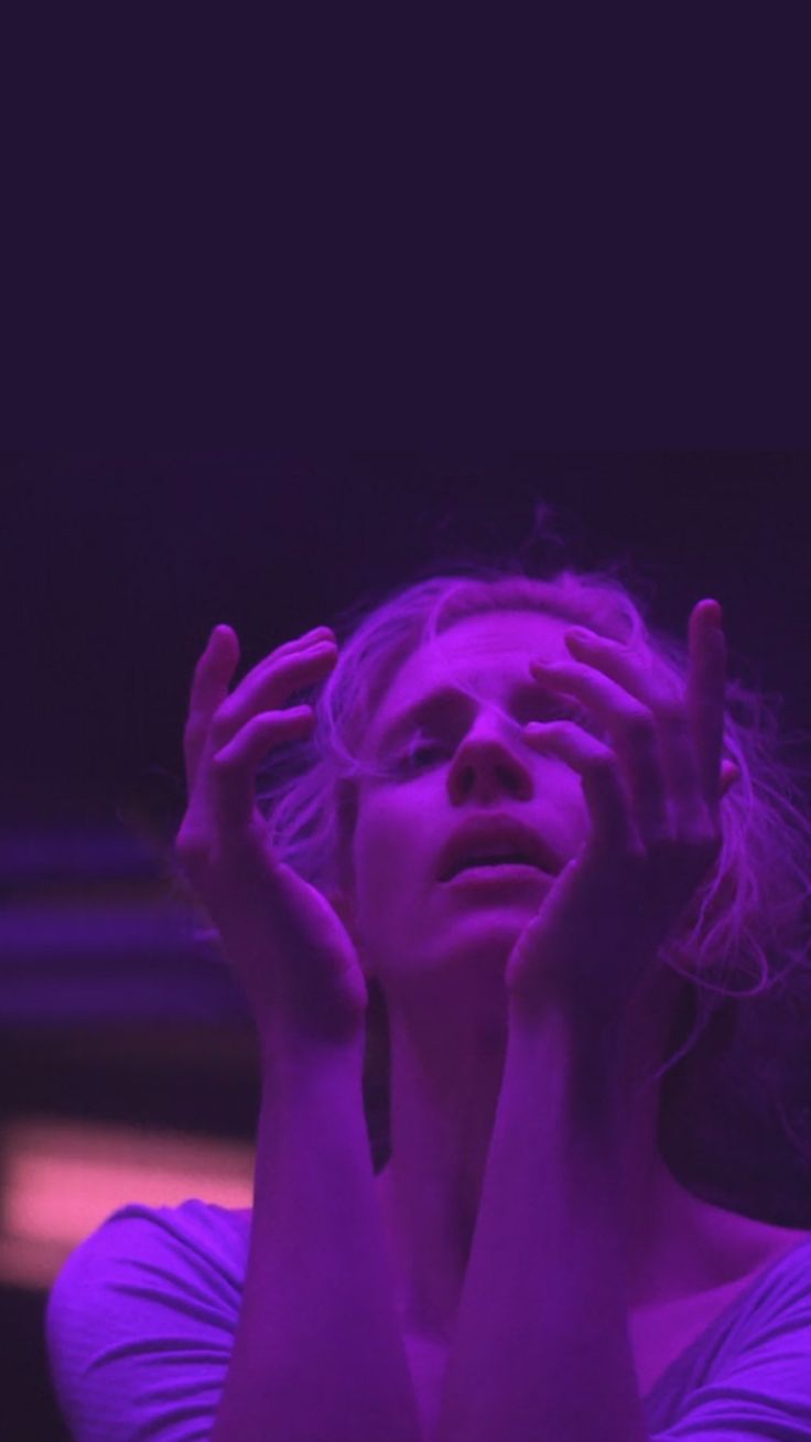 a woman holding her hands to her face in front of purple light with one hand on her head