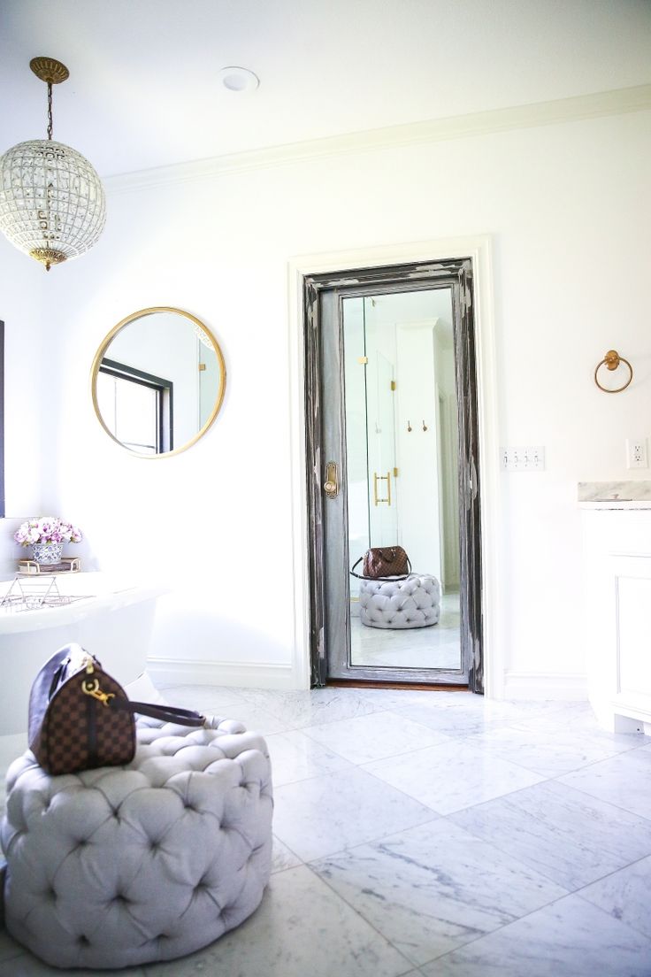 a white bathroom with a round ottoman in the middle and a mirror on the wall