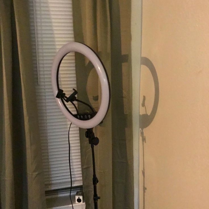 a white ring light sitting on top of a tripod in front of a window